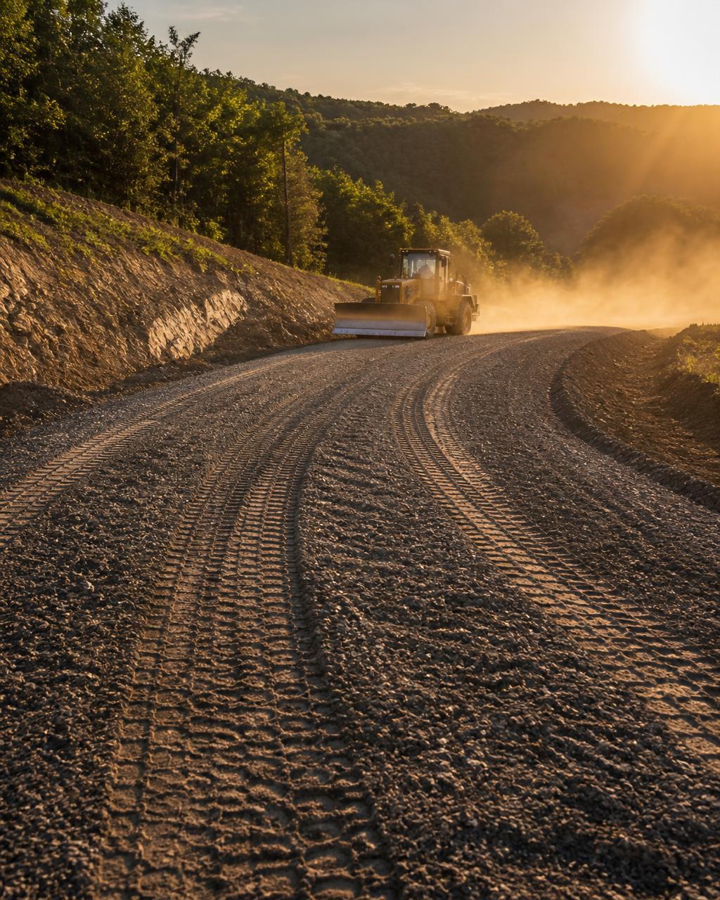 Freshly graded gravel roadbed at golden hour with a bulldozer working in the distance